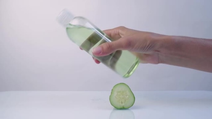 女人的手，把化妆品白色塑料瓶与新鲜的绿色黄瓜片在白色背景上。