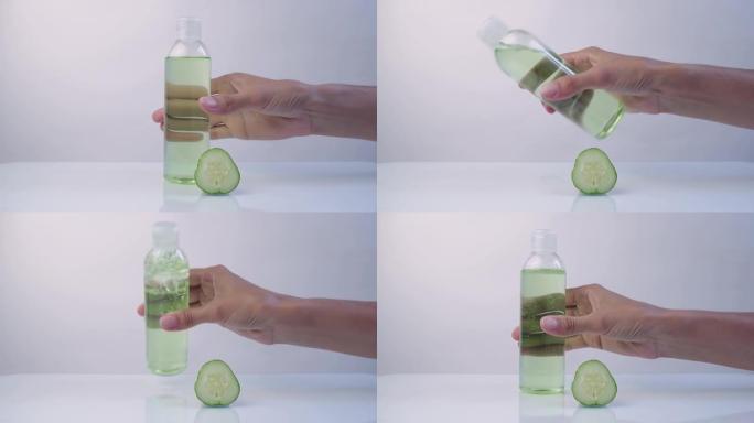 女人的手，把化妆品白色塑料瓶与新鲜的绿色黄瓜片在白色背景上。