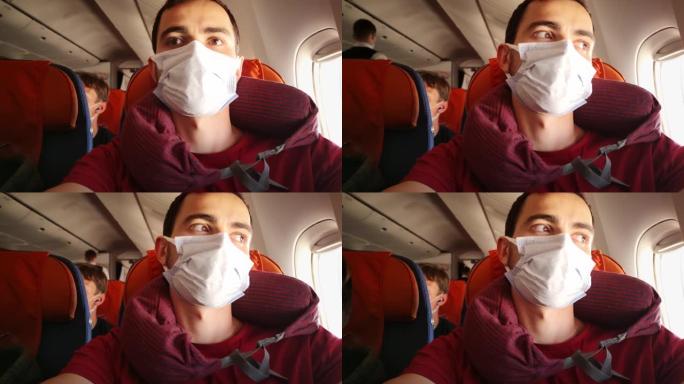年轻的白人男子戴着医用口罩和颈枕坐在飞机内，看着
