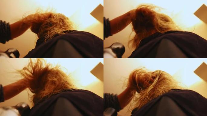 理发师吹干她客户刚洗过的头发。她用手穿过头发以松开头发。相机从下面看
