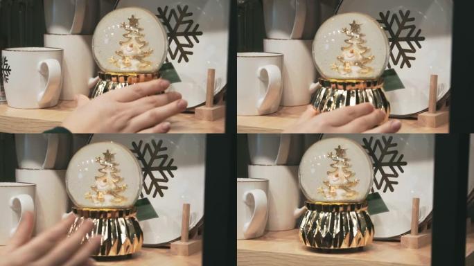 女性的手把漂亮的圣诞雪球放在商店的架子上，慢动作。带有圣诞树和雪人的金色玻璃雪球。