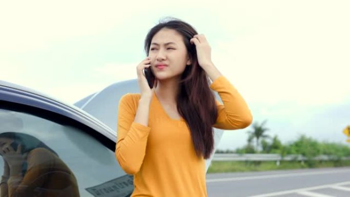 年轻的亚洲妇女在路上抛锚了汽车，她感到严肃和压力很大。找人帮忙。使用智能手机呼叫紧急援助或保险服务。