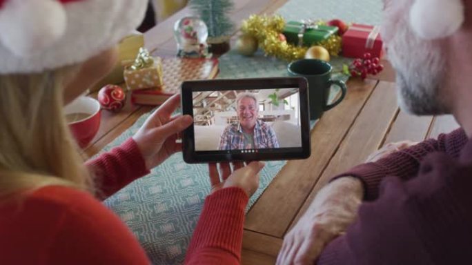 白人夫妇戴着圣诞老人帽子，使用平板电脑与屏幕上的男人进行圣诞节视频通话