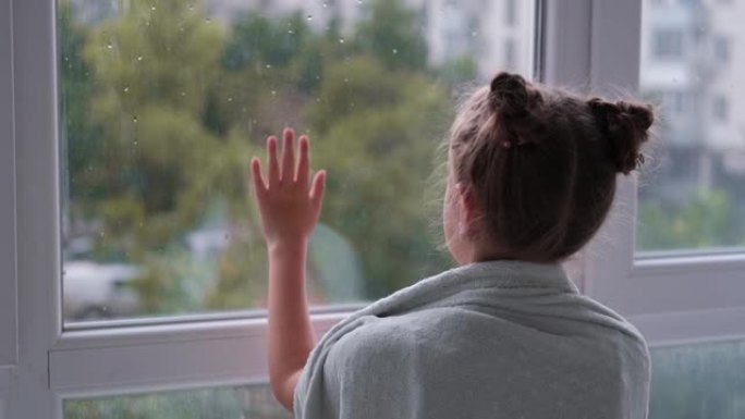 女孩站在窗前，看着雨。孩子在窗前悲伤。