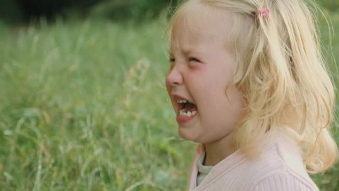 悲伤的金发小女孩在公园里泪流满面