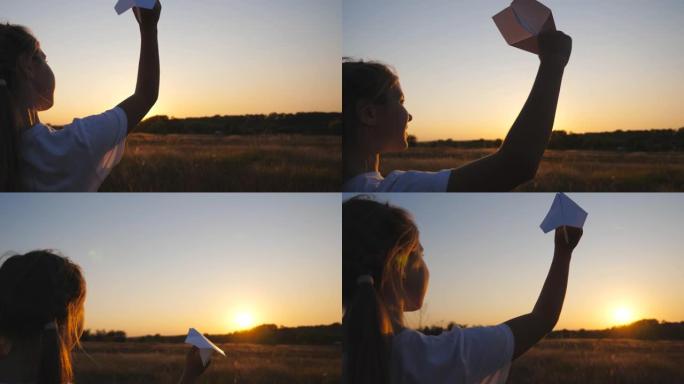 快乐的小女孩站在草地上，手里拿着一架纸飞机。日落背景下，小女孩在草地上玩玩具飞机。无忧无虑的孩子在大