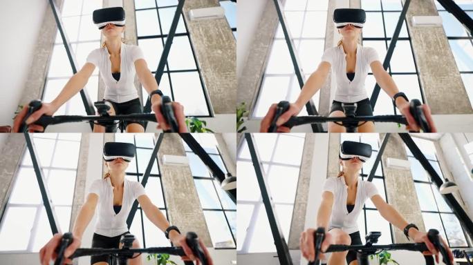 戴VR眼镜的年轻女性正在踩踏室内自行车教练。工作室公寓，厨房。在家进行日常训练。特写，慢动作，低角度