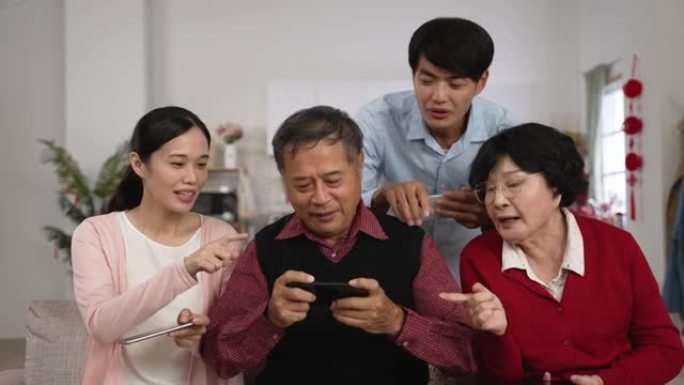 穿着红色衬衫的年迈的父亲在玩手机游戏时挥舞着双手，感到恼火，因为春节期间其他家人在家里指着他唠叨。