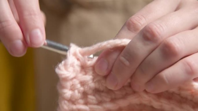一个高加索女孩做钩针编织的年轻女性手的特写，展示了如何正确编织。浅景深。高动态范围。