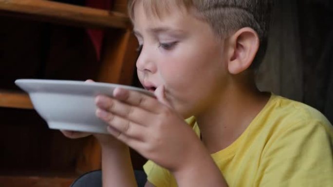 肖像。一个穿黄色衬衫的十几岁男孩吃汤。他在碗的边缘吃完食物。健康自制食品概念