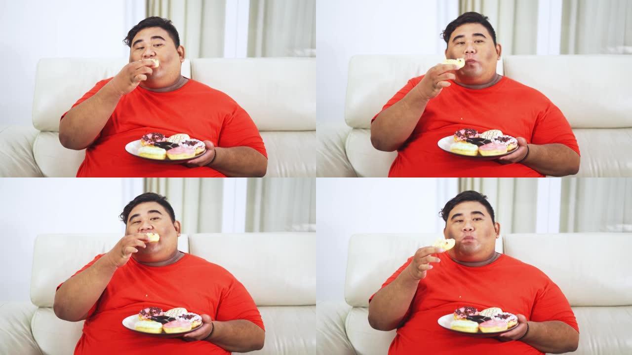 肥胖男子在沙发上吃一盘甜甜圈