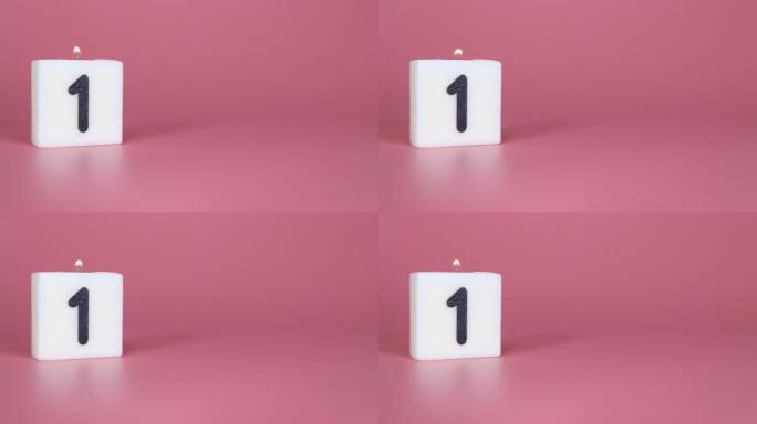 一根方形蜡烛，上面写着数字1在庆祝生日或周年纪念日的粉红色背景上被点燃和吹灭