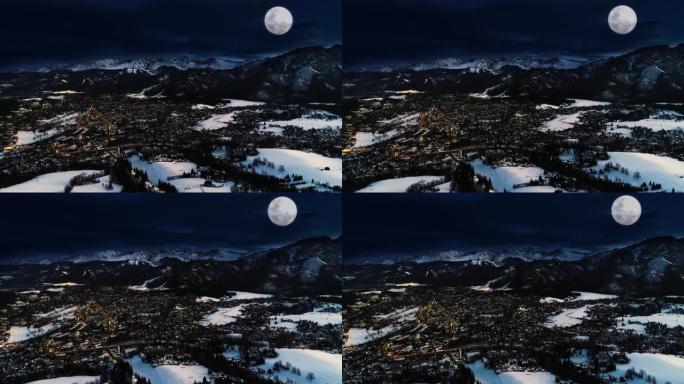 冬夜的山脉，鸟瞰图。神奇的冬天，圣诞村景观。被雪、白色山脉、滑雪胜地和耀眼的大月亮覆盖的高山城市。