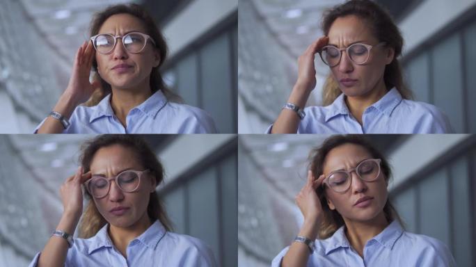 严重集中的非裔美国妇女在眼镜上感到头痛和太阳穴痉挛，按摩额头，情绪倦怠，在嘈杂的环境中工作，与天气有