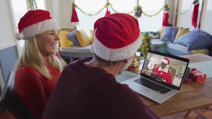 带着圣诞老人帽子微笑的高加索夫妇使用笔记本电脑进行圣诞视频通话屏幕上的圣诞老人