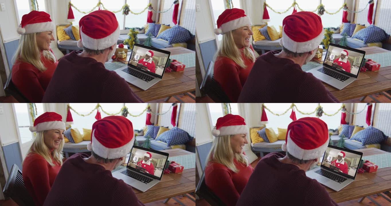 带着圣诞老人帽子微笑的高加索夫妇使用笔记本电脑进行圣诞视频通话屏幕上的圣诞老人
