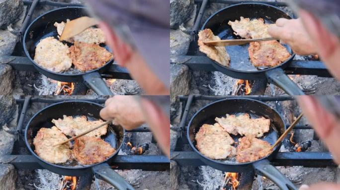 男子在煎锅里用油煮炸猪排，在户外火上，肥肉
