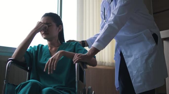 在医院，一个坐在轮椅上过度劳累的年轻女子闭上眼睛抽泣。医生让她放心，并与她交谈，看看她是否需要任何帮
