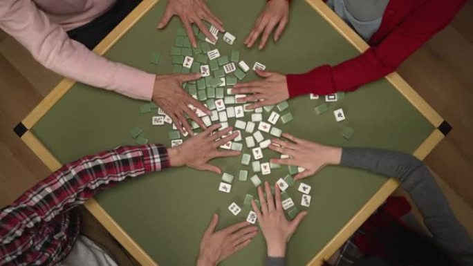 顶部角度拍摄的家庭的手在绿色的桌子上混合面朝下的麻将牌，而在中国除夕在家里玩瓷砖游戏