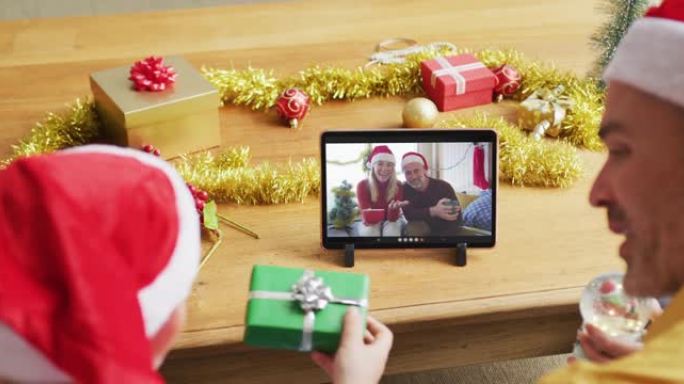 戴着圣诞老人帽子的高加索父子使用平板电脑与家人在屏幕上进行圣诞节视频通话