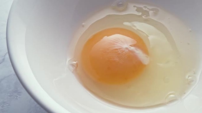 人打碎了一个生鸡蛋，鸡蛋掉进了一个白色的碗里。