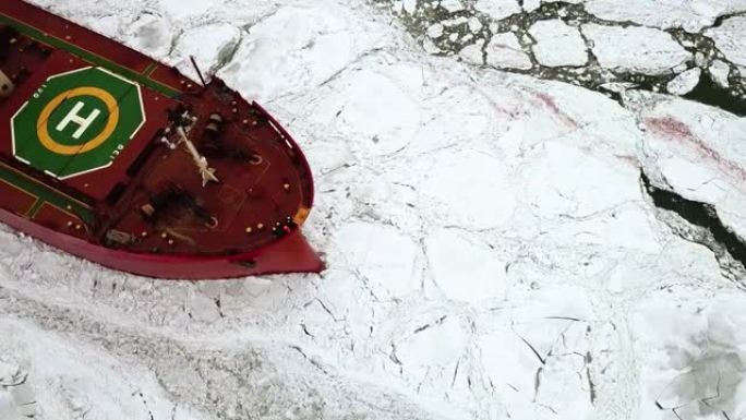 无人机自上而下史诗般的红色钢破冰船油轮打破冬季冰冻的大海，克服。船首漂浮在浮冰中。巨大的白色冰块