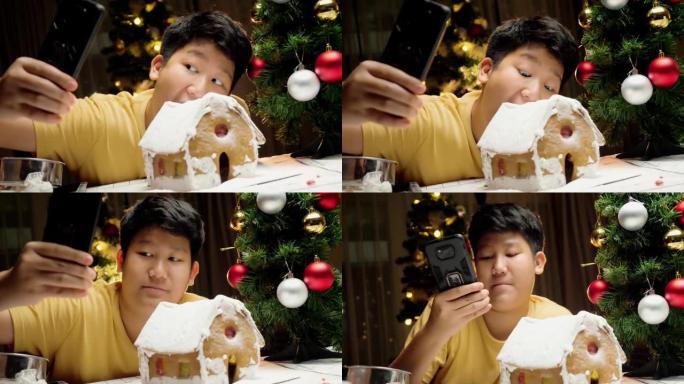 亚洲男孩自拍与姜饼屋完成后，圣诞节庆祝生活方式概念。