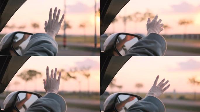 自由女孩的手从窗外骑着汽车风迎面。概念车在路上旅行。女孩伸出她的手走出车窗阳光刺眼的夕阳。快乐和自由