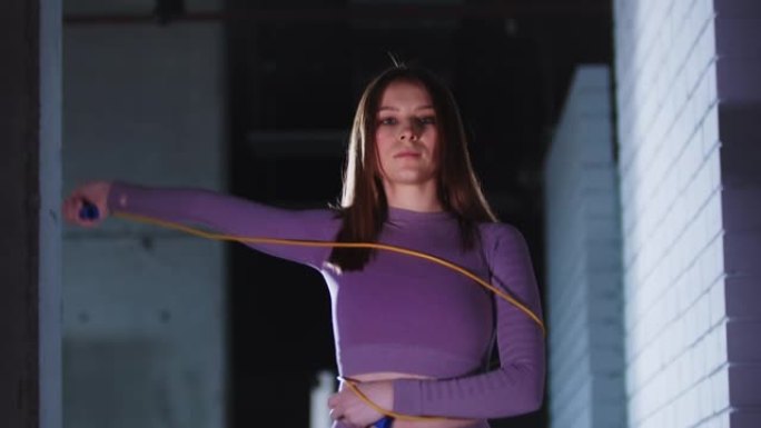 穿着紫色运动服的年轻美女玩着跳绳，看着镜头