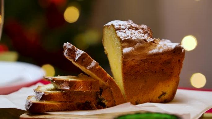 传统的自制蛋糕切成薄片放在节日的桌子上。背景模糊，圣诞树上闪烁着灯光。新年快乐。冬季庆祝活动的完美镜