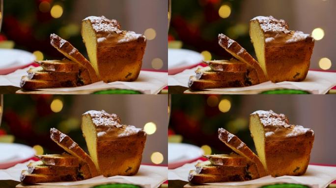 传统的自制蛋糕切成薄片放在节日的桌子上。背景模糊，圣诞树上闪烁着灯光。新年快乐。冬季庆祝活动的完美镜