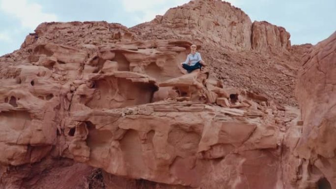 沙漠中带有红色岩石地层的瑜伽姿势中的女人的和平无人机视图