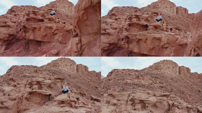 沙漠中带有红色岩石地层的瑜伽姿势中的女人的和平无人机视图