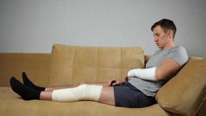 男子坐在膝盖受伤和前臂骨折的沙发上