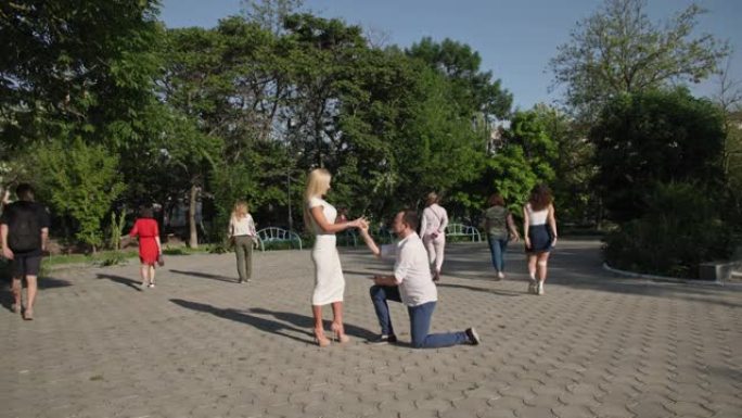 幸福的夫妻，恋爱中的男人向年轻美丽的女人要约，并在公园里一群人的手指上戴上戒指