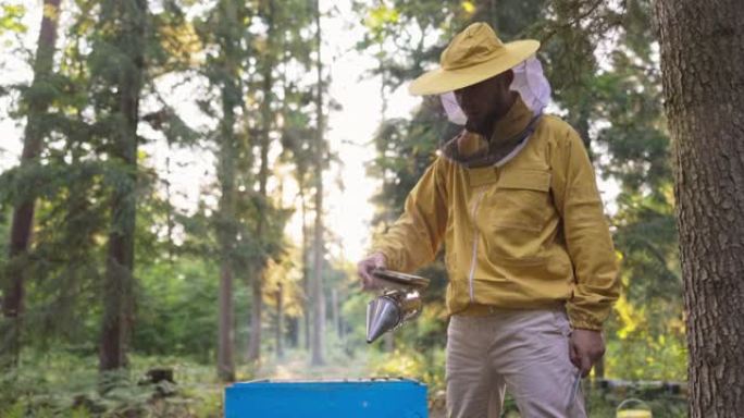 一名身穿防护服，头上戴着蚊帐的养蜂人在蜂巢上喷出白烟，蜂巢上有特殊配件，养蜂场吸尘器，在森林中工作