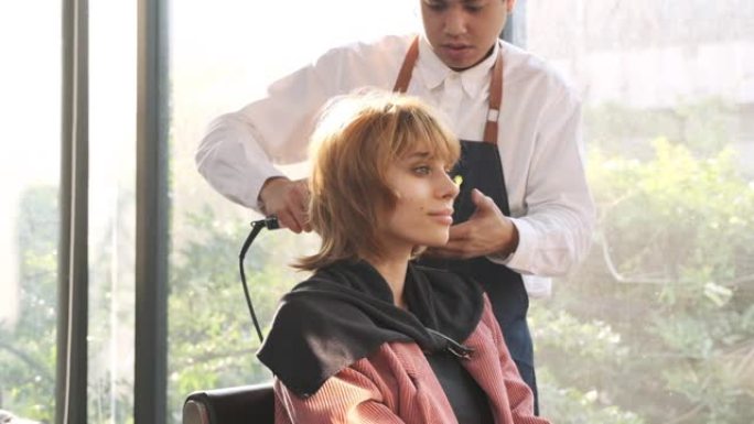 美发师在美容院用小吹风机为美丽的高加索女人做头发。