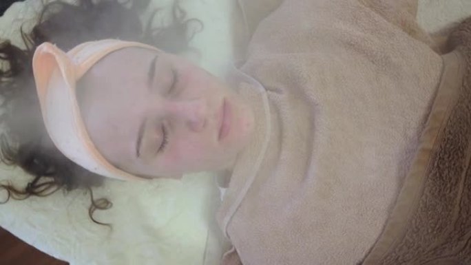 闭着眼睛的年轻女子的特写肖像，脸上有热蒸汽处理。痤疮问题治疗