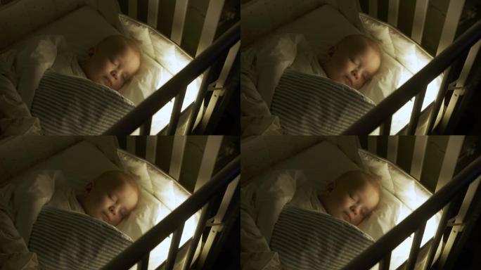 婴儿襁褓躺在婴儿床里，9个月的男婴睡在夜灯下。