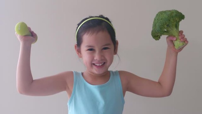 快乐健康的混合亚洲女孩举起西兰花和哑铃，儿童健康概念