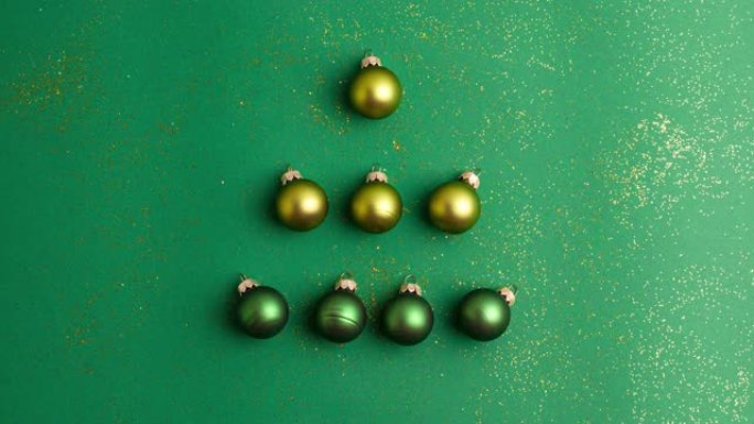 另类的绿色和黄色圣诞球在翡翠绿色的背景上制成带有金色闪光的树。定格动画圣诞假期和呈现概念平铺
