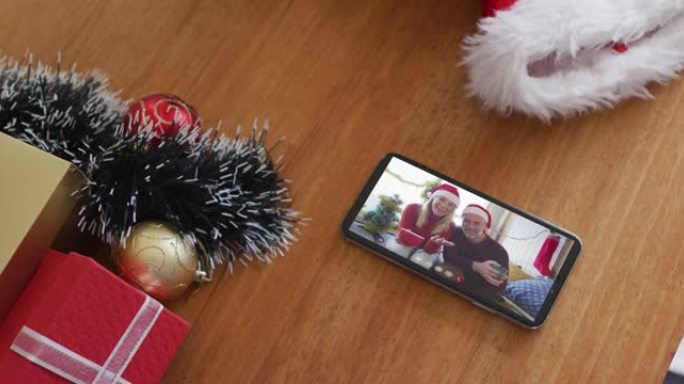 微笑的白人夫妇戴着圣诞老人的帽子，在智能手机上播放圣诞节视频通话