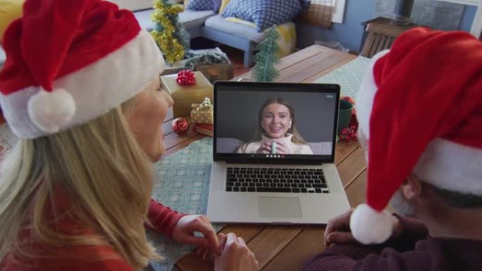 白人夫妇戴着圣诞老人帽子，使用笔记本电脑与屏幕上的女人进行圣诞节视频通话