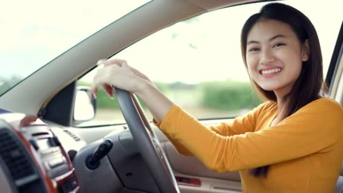 年轻漂亮的亚洲女性得到新车。她看着窗外非常高兴和兴奋。灿烂的日子里，微笑的女性驾驶车辆在路上