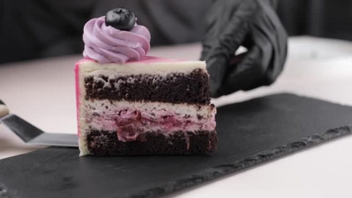 糕点师傅的手的特写镜头，将一块蓝莓装饰的海绵蛋糕放在黑色基材上