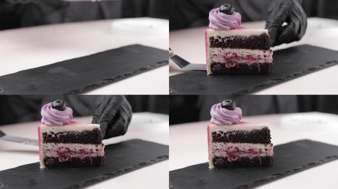 糕点师傅的手的特写镜头，将一块蓝莓装饰的海绵蛋糕放在黑色基材上