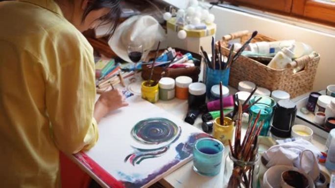 在她凌乱的艺术工作室里，女性高加索艺术家在画布上绘画