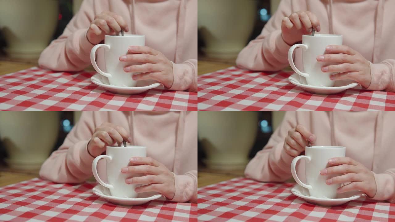 女孩在晚上坐在餐桌旁的咖啡馆里的陶瓷杯上用勺子混合糖或甜叶菊