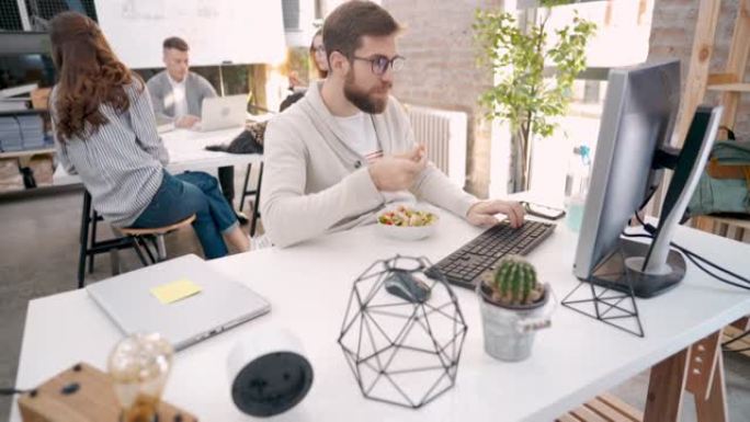 专注于白人的男性企业家，一边吃沙拉一边在电脑上工作