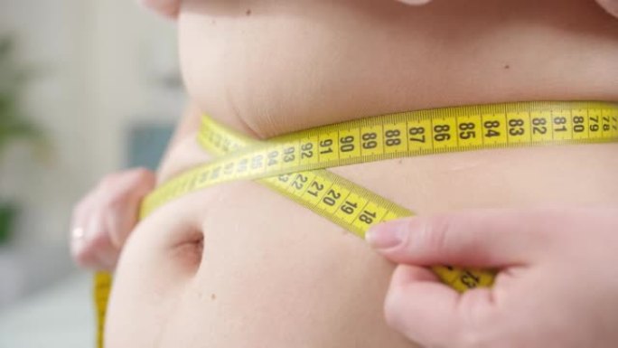 女人用黄色的卷尺测量她肥胖的腹部或腰部。节食的概念，不健康的生活方式，超重和肥胖
